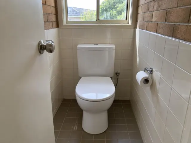 Clean white toilet in a tiled bathroom with brick walls and a window in Meadowbank