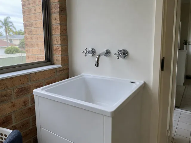 White laundry sink with chrome taps on a brick and painted wall in Putney